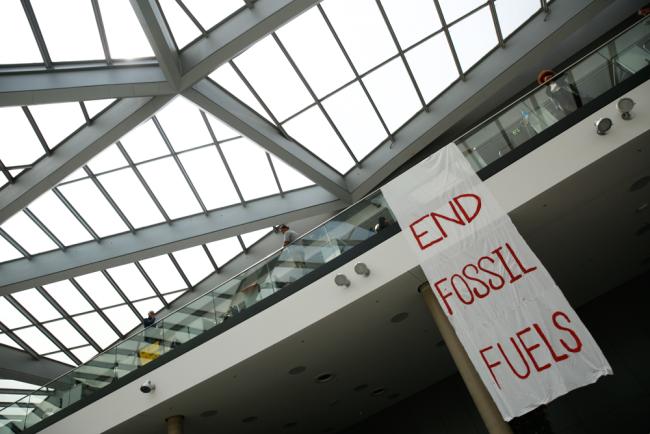 As the COP28 President-designate arrives at the venue, members of civil society drop a banner from the gallery of the main entrance, calling for the end to fossil fuels